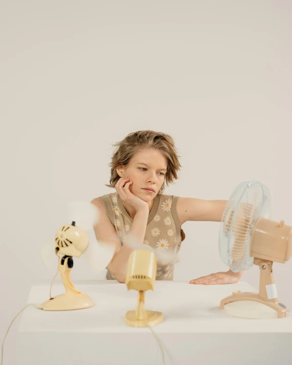 a woman sitting at a table with a fan, inspired by Anna Füssli, pexels contest winner, patricia piccinini, air conditioner, art toys on a pedestal, sydney sweeney