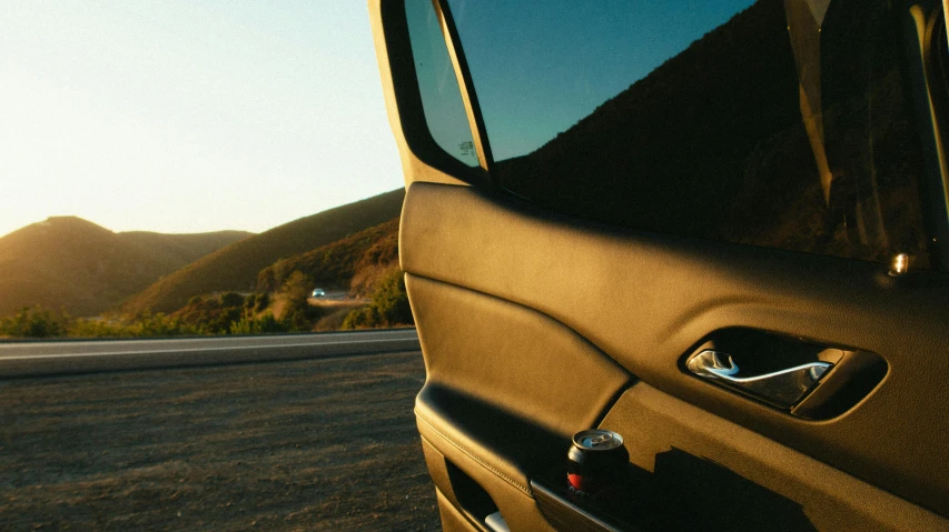 a car is parked on the side of the road, unsplash, photorealism, malibu canyon, window open, golden hour closeup photo, leather interior