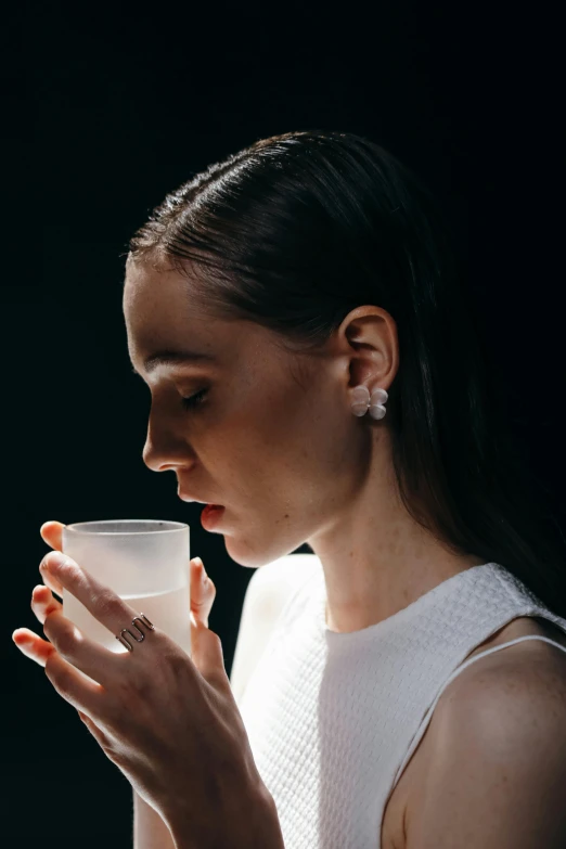 a woman is drinking a glass of water, inspired by Elsa Bleda, with white skin, dark backdrop, secret tea society, skincare