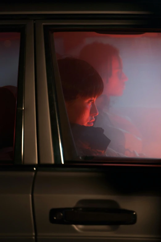 a person sitting in a car looking out the window, inspired by Nan Goldin, realism, still from stranger things, with red haze, lee madgwick & liam wong, person in foreground