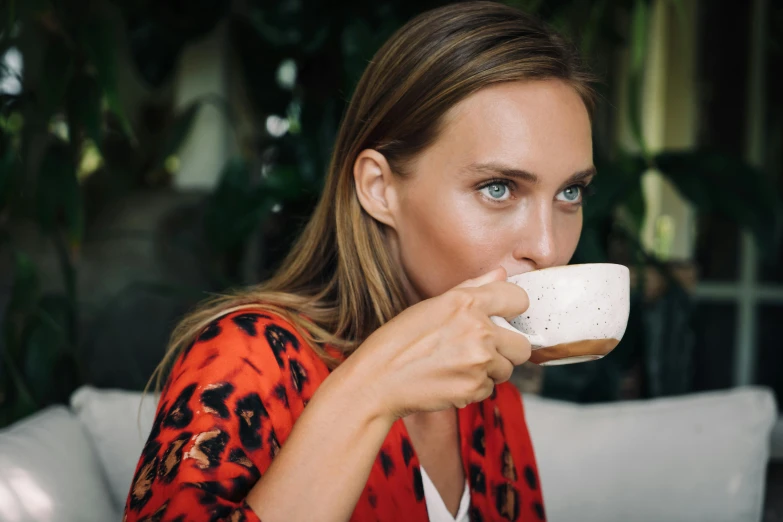 a woman sitting on a couch drinking out of a cup, a portrait, by Julia Pishtar, pexels contest winner, happening, robe. perfect face, camilla luddington, manuka, close up of a blonde woman