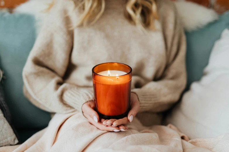 a woman sitting on a couch holding a candle, pexels, autumnal colours, soft grey and red natural light, vibrant orange, made of glazed