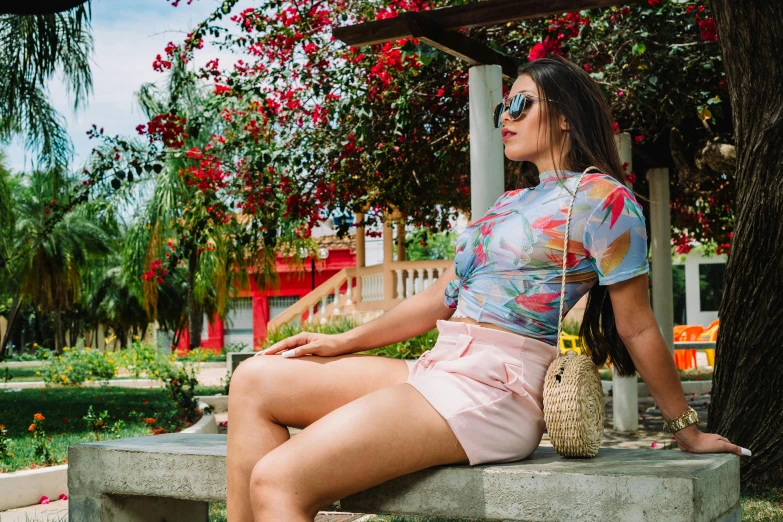 a woman sitting on top of a cement bench, croptop and shorts, shades of pink and blue, colombian, profile image