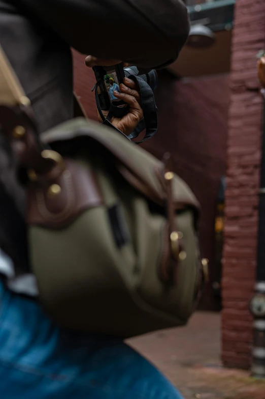 a man walking down a street holding a camera, by Andrew Domachowski, carrying a saddle bag, green and brown tones, slide show, detail shot