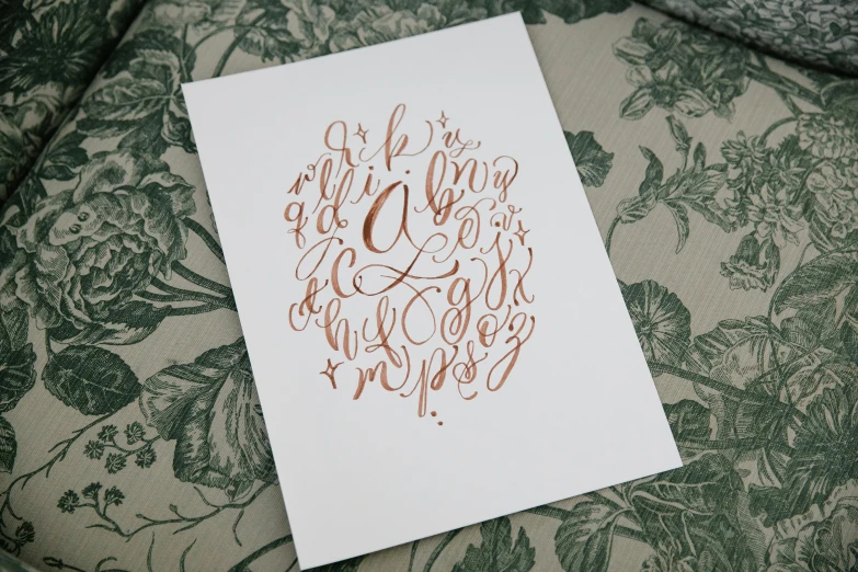 a close up of a piece of paper with writing on it, a screenprint, inspired by Zsolt Bodoni, unsplash, letterism, rose gold, o pattern, arabian calligraphy, nursery poster