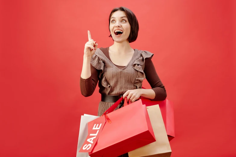 a woman holding shopping bags and pointing up, pexels contest winner, red theme, brown, surprising, small