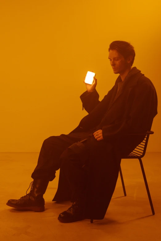 a man sitting in a chair holding a cell phone, an album cover, irrdescent glow, ignant, zachary corzine, catalog photo