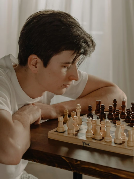 a man sitting at a table playing a game of chess, a colorized photo, by Adam Marczyński, unsplash contest winner, realism, looking to his side, an epic non - binary model, profile image, ( ( theatrical ) )