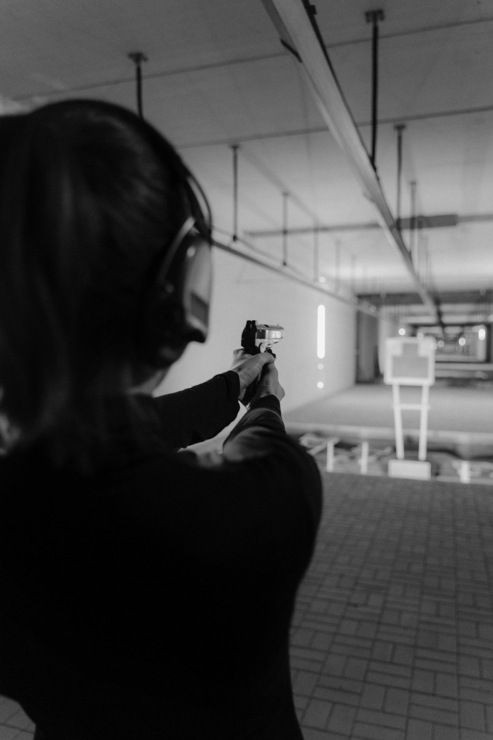 a black and white photo of a woman shooting a gun, over the shoulder perspective, trapped in the backrooms, instagram picture, taken with canon 5d mk4