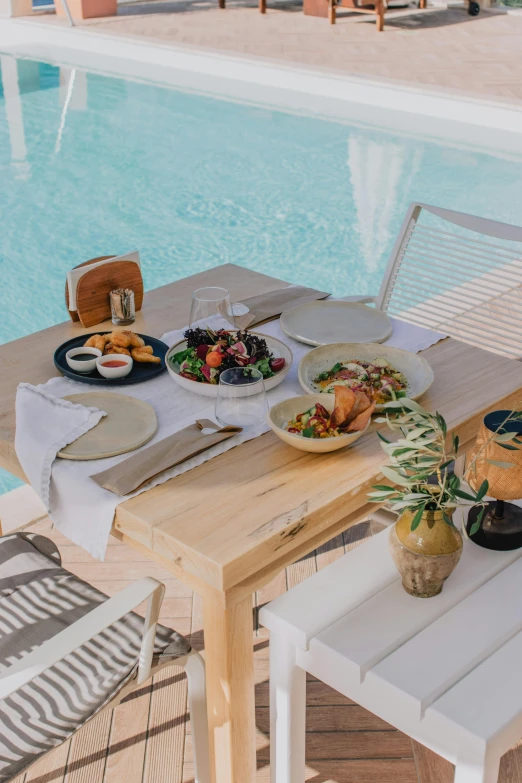 a wooden table topped with plates of food next to a swimming pool, profile image, sol retreat, full frame image