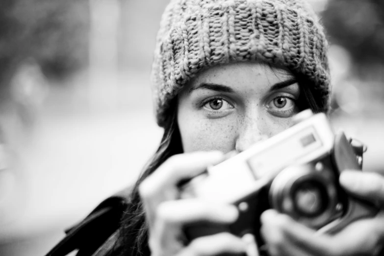a black and white photo of a woman holding a camera, by Etienne Delessert, unsplash, wearing wool hat, eyes, medium format, cute photograph