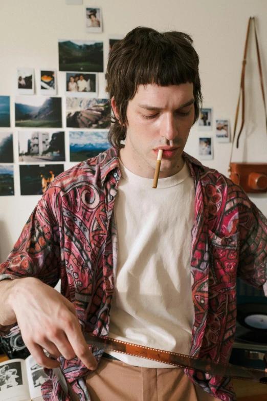 a man standing in a room with a cigarette in his mouth, an album cover, by Adam Dario Keel, trending on unsplash, hyperrealism, cottagecore hippie, bryan lee o'malley, smoking a bowl of hash together, patterned clothing