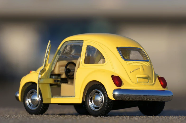 a yellow toy car sitting on top of a parking lot, unsplash, photorealism, beetle, highly detailed model, rear-shot, 2070s