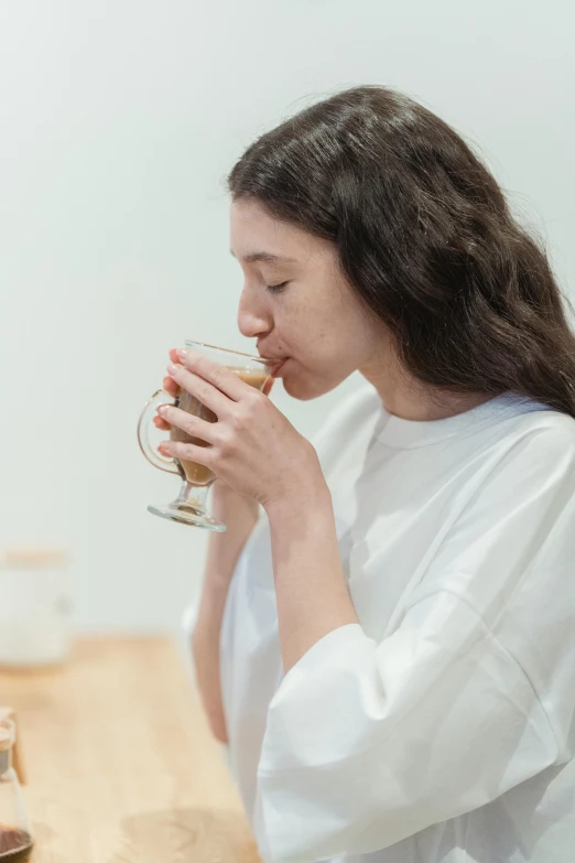 a woman sitting at a table drinking a cup of coffee, diffused natural skin glow, yasumoto oka, profile image, manuka