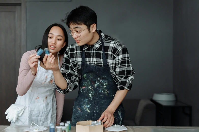 a man and a woman looking at a cell phone, a hyperrealistic painting, pexels contest winner, wearing an apron, modelling clay, asian male, crafting