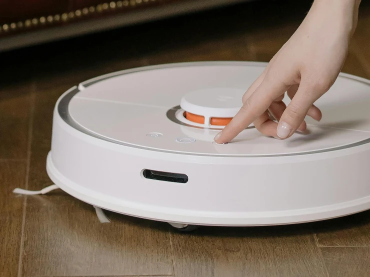 a person using a robotic vacuum cleaner on the floor, by Julia Pishtar, trending on reddit, titanium white, mkbhd, holding a tower shield, hand on table