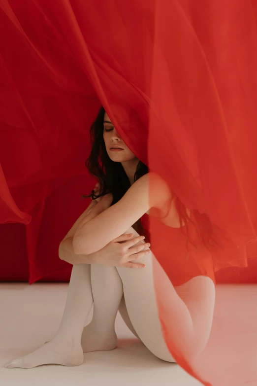 a woman sitting in front of a red curtain, flowing material, soft skin, unsplash contest winning photo, red body suit