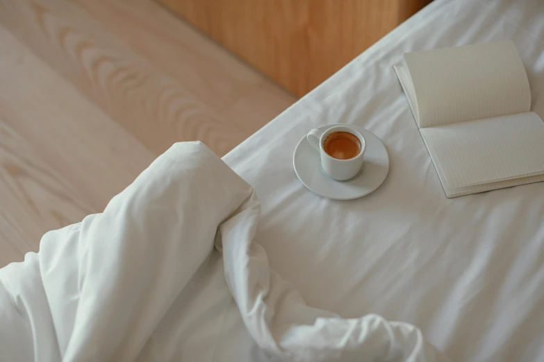 a cup of coffee and a book on a bed, by Elsa Bleda, unsplash contest winner, happening, white tablecloth, beds, john pawson, thick lining