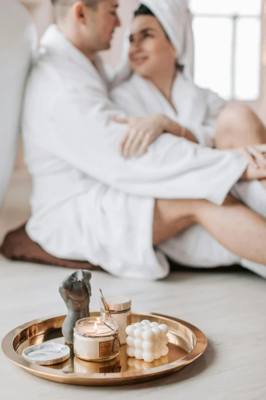 a man and a woman sitting on a bed next to each other, trending on pexels, aestheticism, wearing white robe, spa, white candles, healing pods