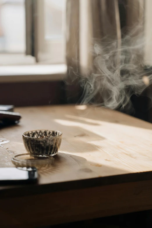 a cup of coffee sitting on top of a wooden table, marijuana smoke, very hazy, botanicals, black whispy smoke