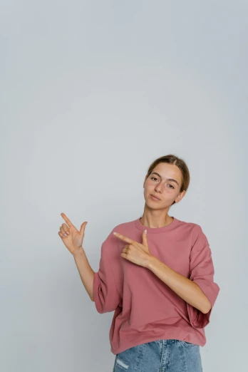 a woman in a pink shirt is pointing at something, trending on pexels, grey backdrop, cinematic, multiple stories, non binary model
