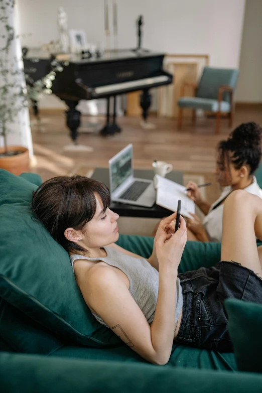 a couple of women sitting on top of a green couch, trending on pexels, goddess checking her phone, with notes, music being played, home office