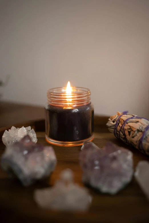 a candle sitting on top of a wooden table, amethyst, obsidian accents, inside a glass jar, soothing