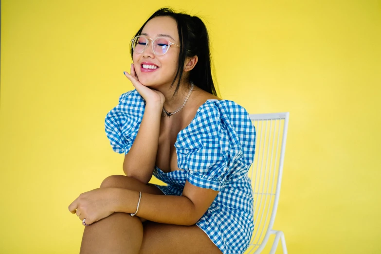 a woman sitting on top of a white chair, inspired by Ruth Jên, trending on pexels, blue checkerboard dress, with square glasses, wearing yellow croptop, avatar image