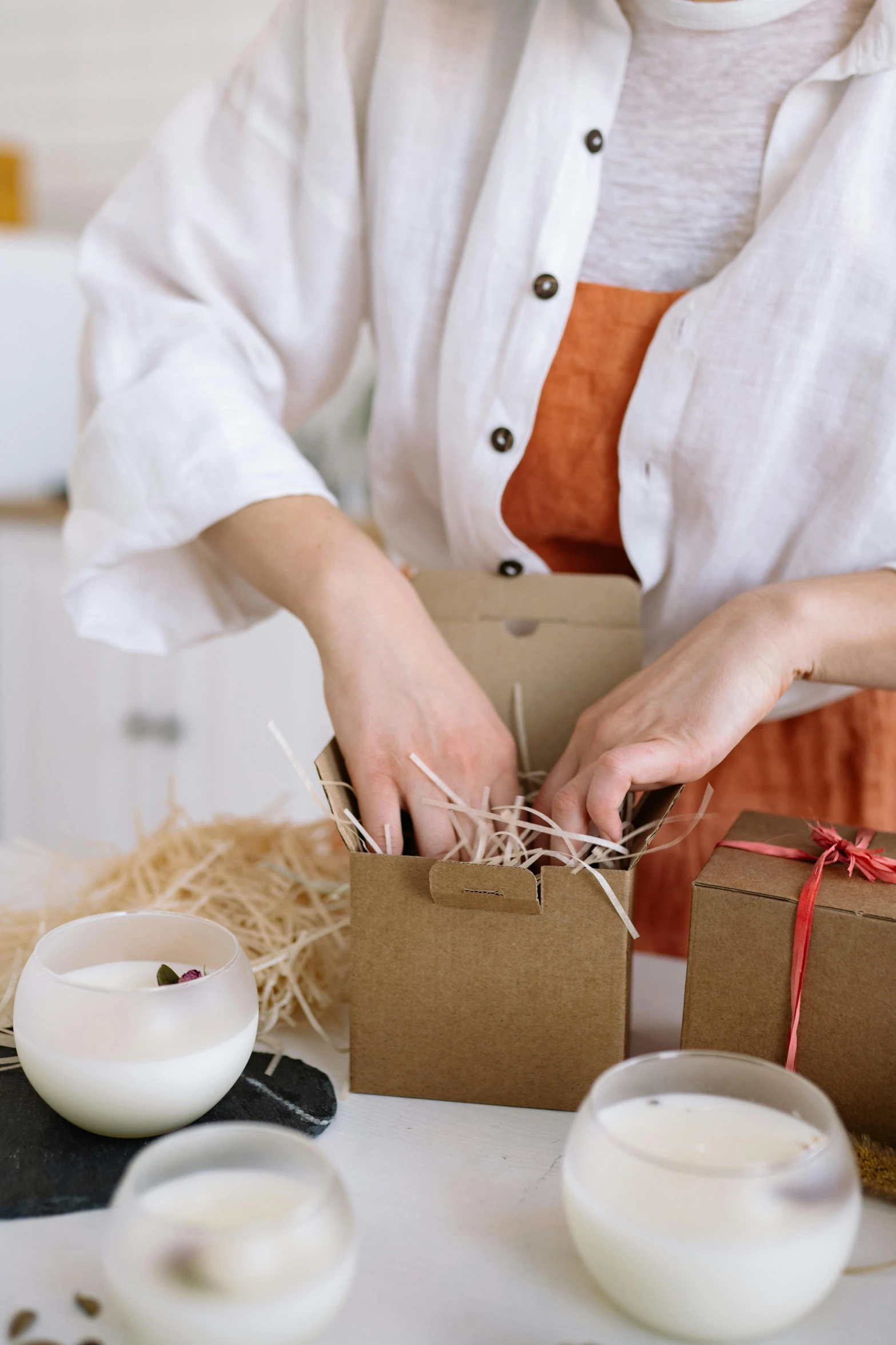 a woman sitting at a table with a box of candles, by Eden Box, white apron, roots and hay coat, holding gift, mid - action