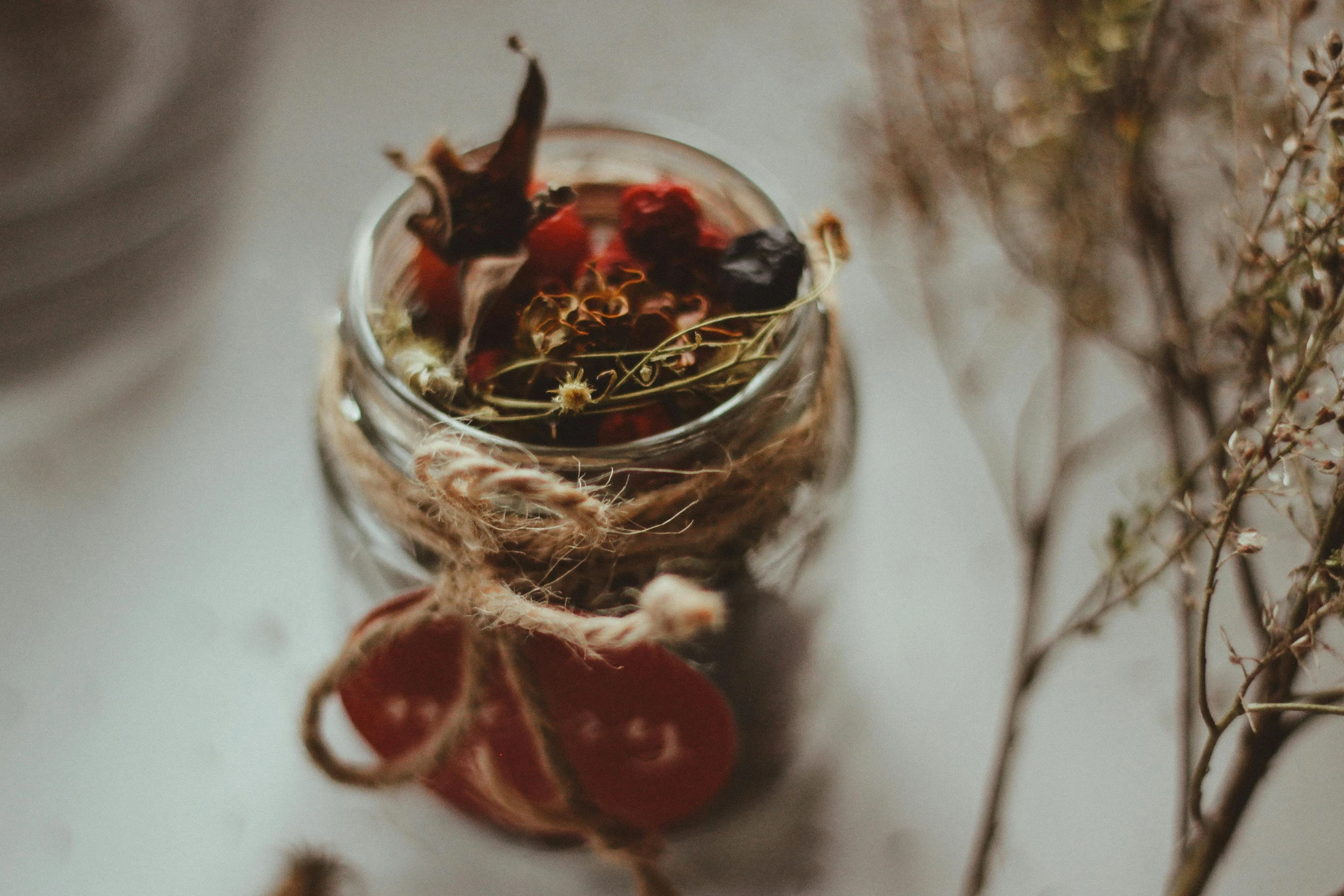 a jar filled with dried fruit sitting on top of a table, by Emma Andijewska, pexels contest winner, renaissance, herbs and flowers, close up shot of an amulet, accents of red, dreamy and ethereal