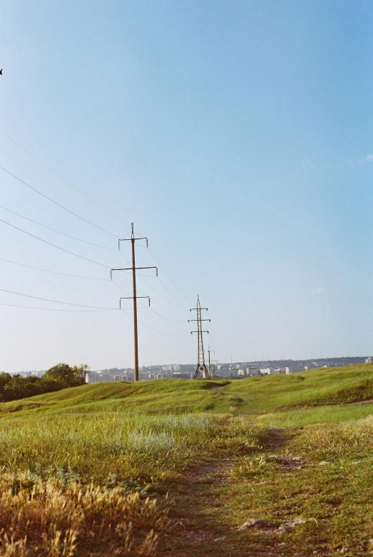 a man flying a kite on top of a lush green field, by Attila Meszlenyi, power lines, stephen shore, panoramic, photo taken on fujifilm superia