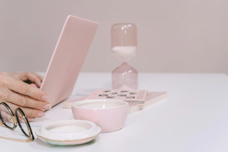 a person sitting at a table with a laptop, a still life, by Carey Morris, trending on pexels, minimalism, light pink, thin porcelain, scales with magic powder, background image