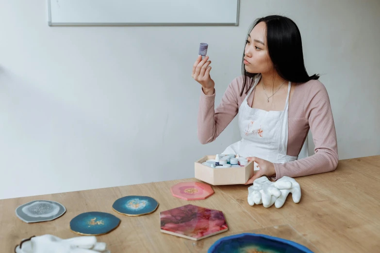 a woman sitting at a table holding a cell phone, an airbrush painting, inspired by Kim Tschang Yeul, pexels contest winner, white ceramic shapes, celestial asthetics, plasticine, product introduction photo