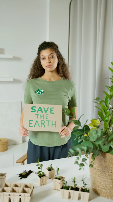 a woman holding a sign that says save the earth, a picture, shutterstock, in a dark green polo shirt, square, lifestyle, woman made of plants