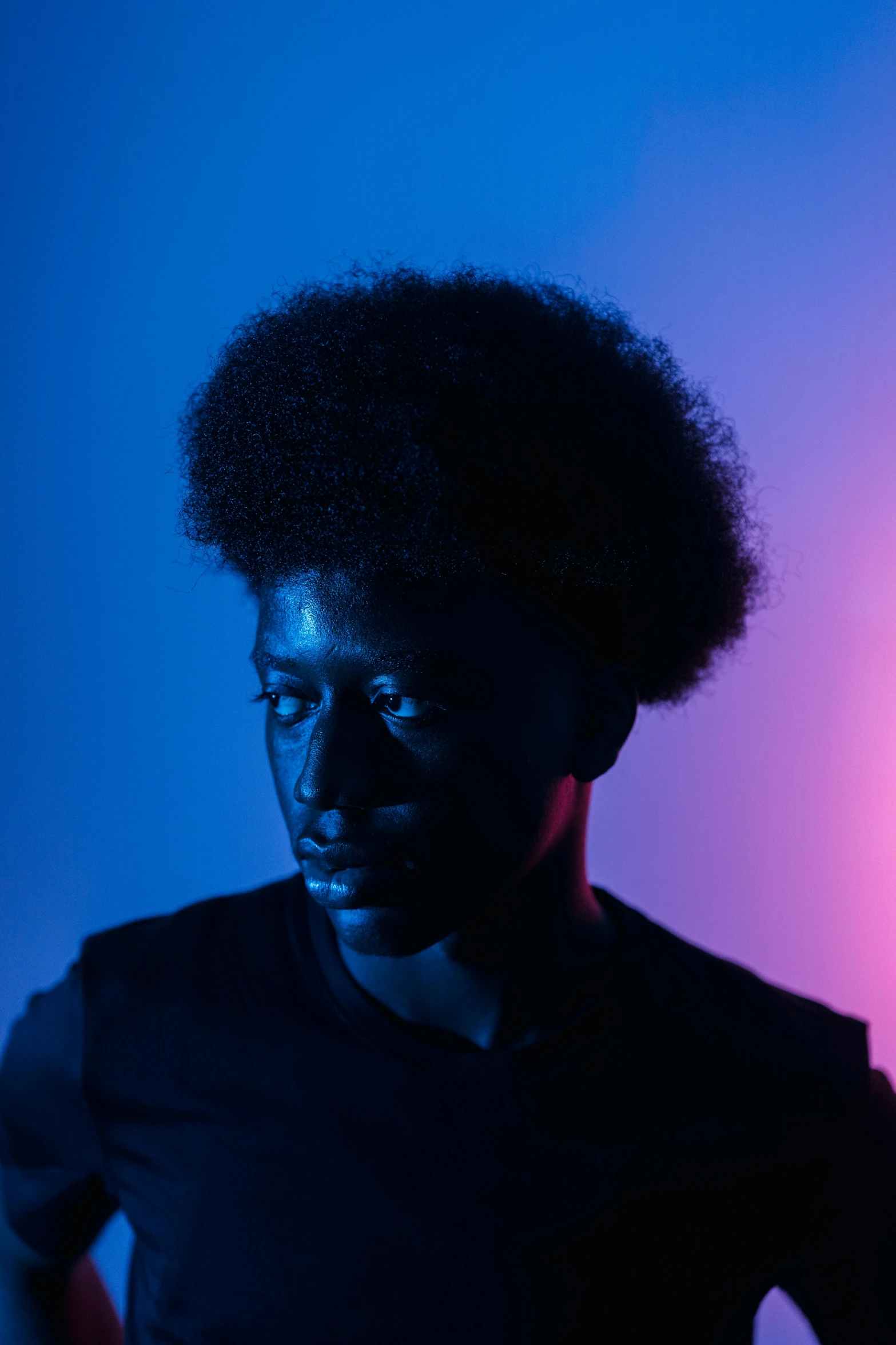 a man standing in front of a blue and pink light, an album cover, by Winona Nelson, pexels contest winner, afrofuturism, black man with afro hair, portrait soft light, monochromatic, shot with sony alpha