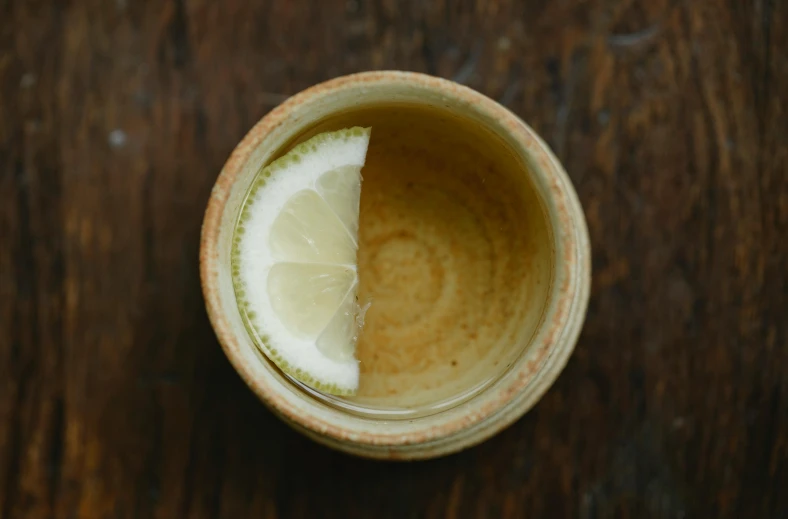 a cup of tea with a slice of lemon in it, by Jessie Algie, trending on unsplash, pottery, with lemon skin texture, moringa juice, half turned around