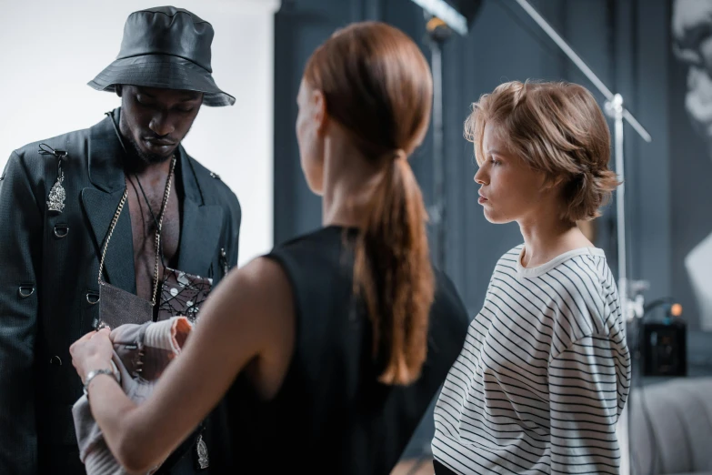 a man standing next to a woman in a room, by Nina Hamnett, pexels contest winner, fashion week backstage, caracter with brown hat, 3 actors on stage, photoshoot for skincare brand