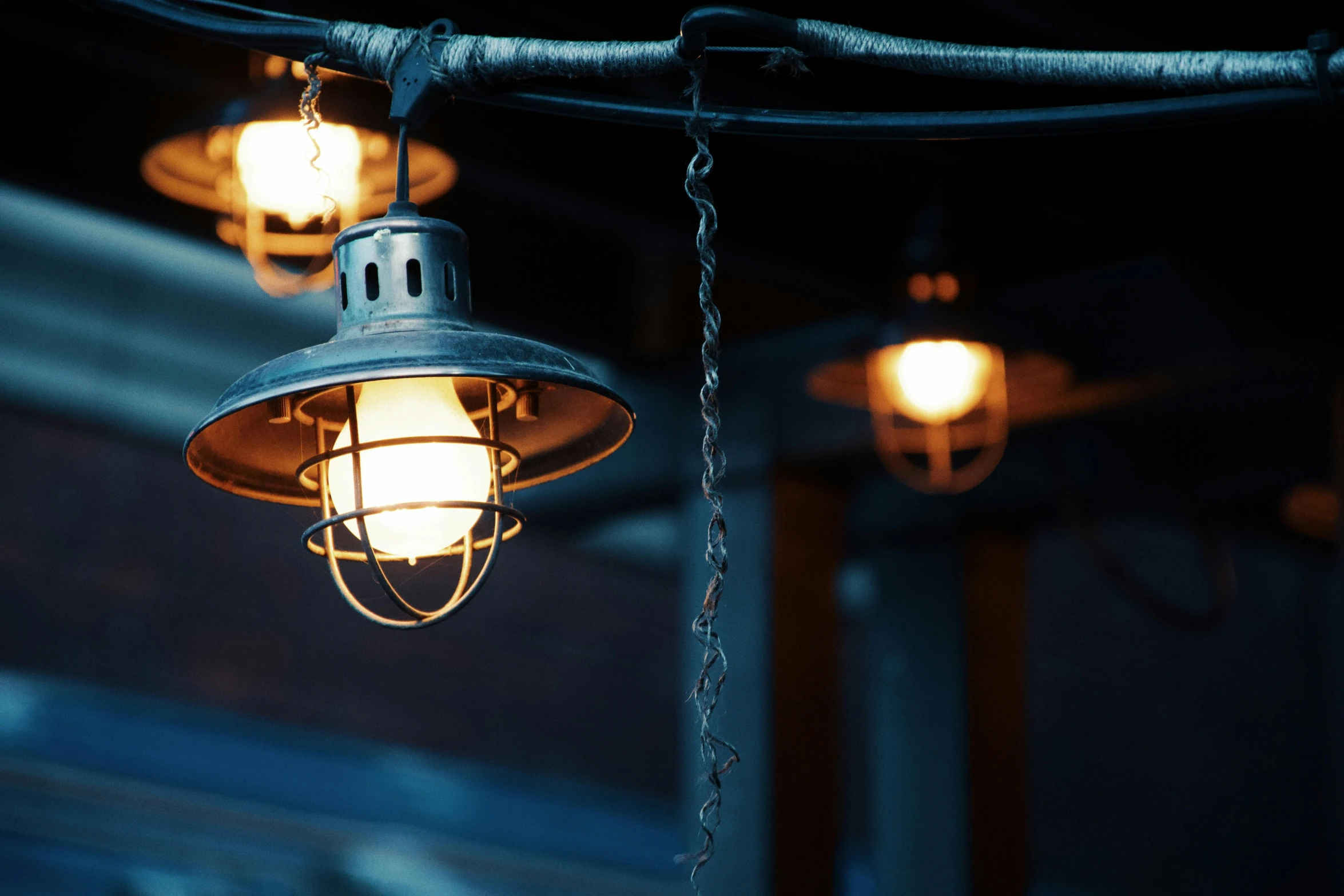 a couple of lights hanging from a ceiling, inspired by Elsa Bleda, unsplash, lanterns on the porch, industrial party, deep blue lighting, poorly lit