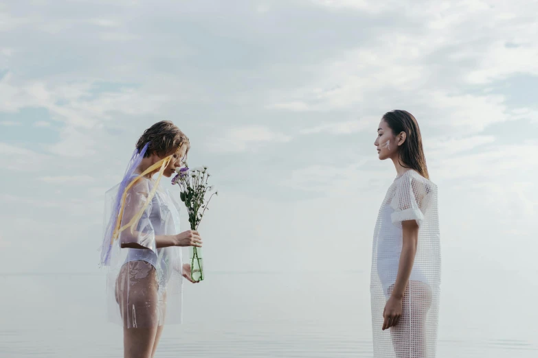 a couple of women standing next to each other on a beach, inspired by Ren Hang, pexels contest winner, romanticism, kind cyborg girl with flowers, translucent dress, concert, ignant