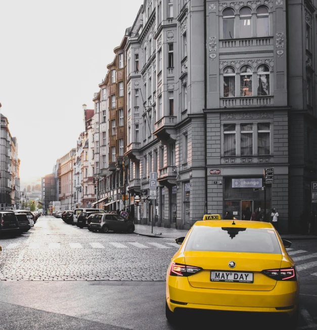 a yellow taxi driving down a street next to tall buildings, by Matija Jama, pexels contest winner, art nouveau, prague in the background, square, bmw, unsplash 4k