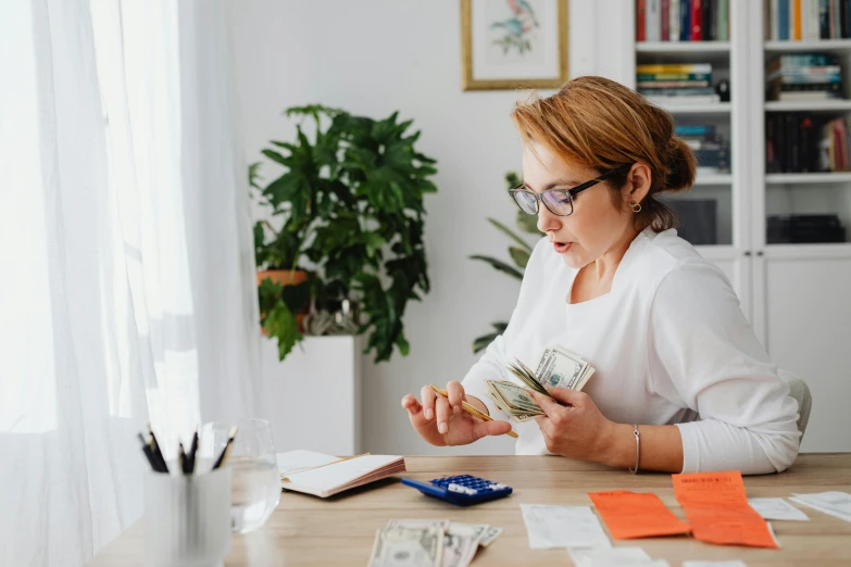 a woman sitting at a table holding a stack of money, pexels contest winner, fan favorite, avatar image, abcdefghijklmnopqrstuvwxyz, studious