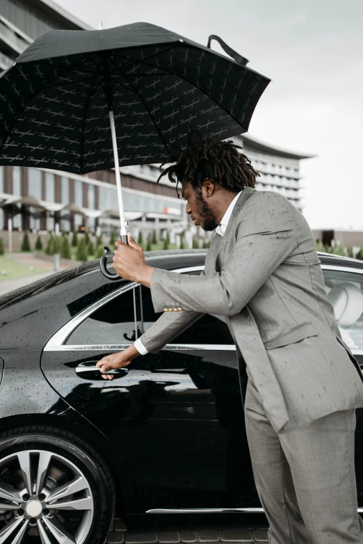 a man standing next to a car holding an umbrella, black luxurious suit, a black man with long curly hair, top selection on unsplash, performing