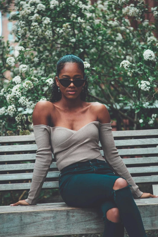 a woman sitting on top of a wooden bench, by Dulah Marie Evans, trending on unsplash, renaissance, fashion model in sunglasses, sexy girl with dark complexion, off the shoulder shirt, accurately portrayed