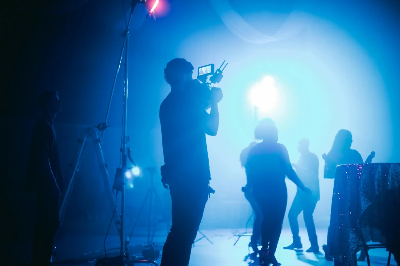 a group of people standing on top of a stage, pexels, video art, cinema studio lights, dramatic blue light, camera footage, ( ( theatrical ) )