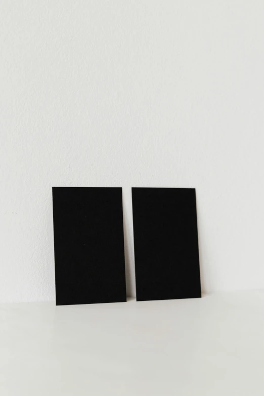 two black books sitting on top of a white table, a minimalist painting, unsplash, solid black #000000 background, placards, ello, real photo