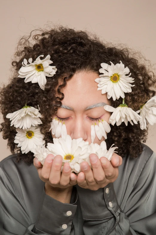 a woman holding a bunch of daisies in front of her face, an album cover, trending on unsplash, aestheticism, mixed race, floating in perfume, androgynous person, porcelain