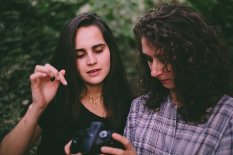 a couple of women standing next to each other, a picture, trending on pexels, taking a picture, brunettes, vhs colour photography, looking her shoulder