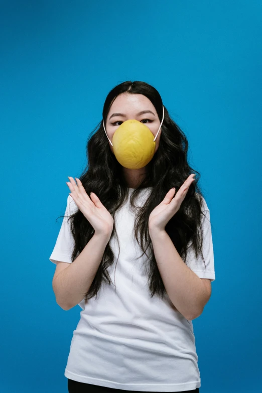 a woman holding a tennis ball in front of her face, an album cover, unsplash contest winner, miranda cosgrove, surgical mask covering mouth, wearing a lemon, studio shoot