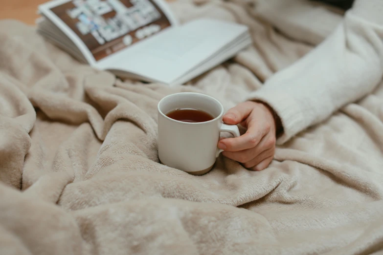 a person holding a cup of coffee on a bed, by Carey Morris, pexels contest winner, manuka, secret tea society, a cold, on a canva