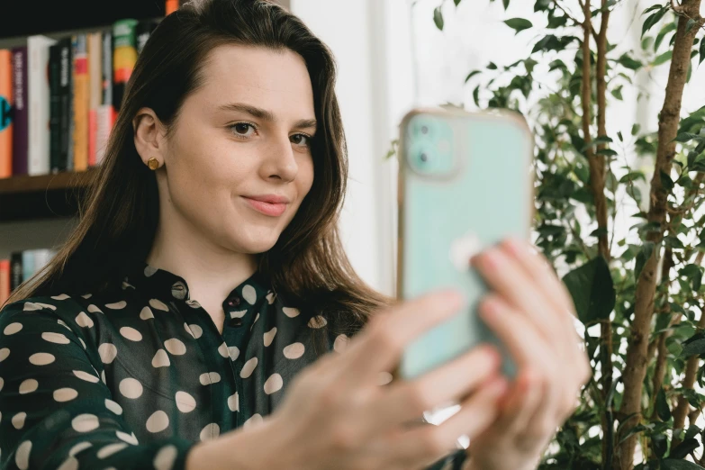 a woman taking a selfie with her cell phone, a picture, trending on pexels, happening, polka dot, girl with brown hair, photoshoot for skincare brand, wearing a green sweater